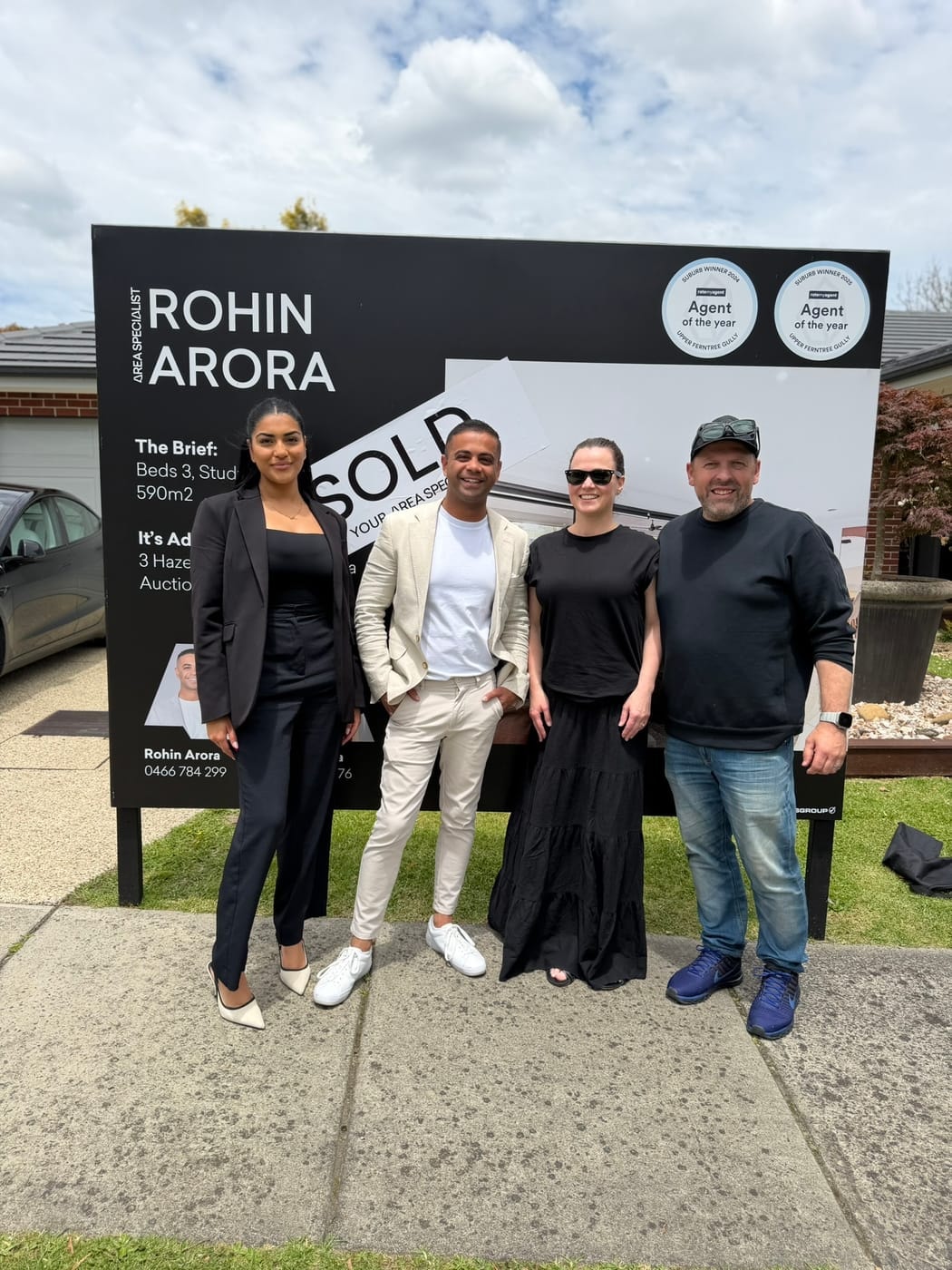 Four people dressed up in front of a SOLD signboard