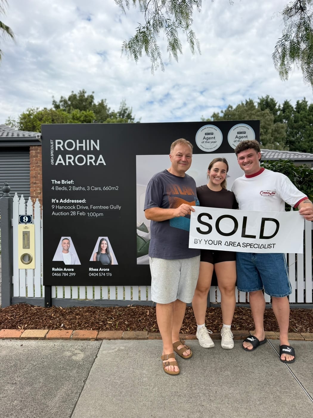 Three people holding up a SOLD sticker in front of the signboard