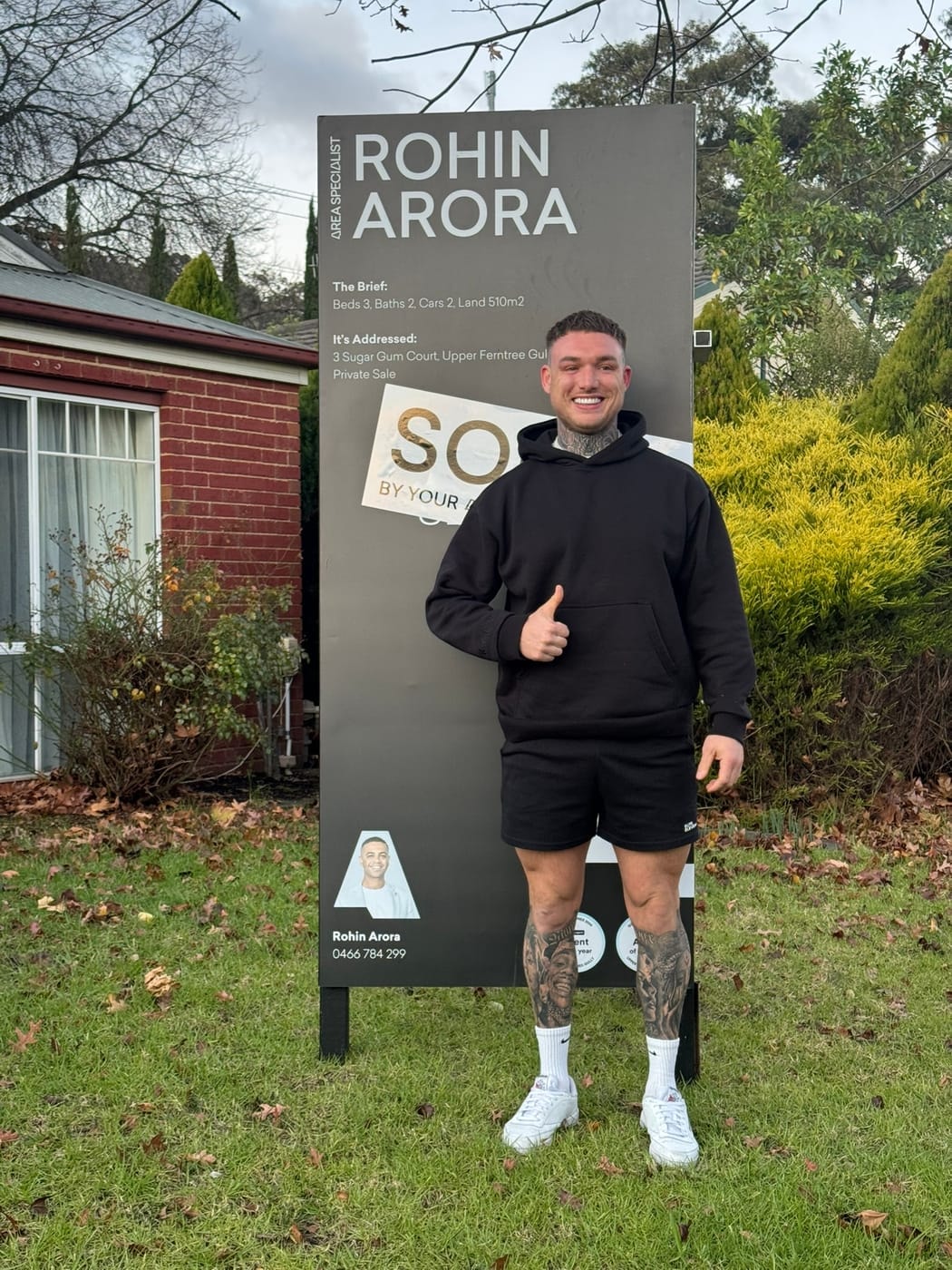 A man giving a thumbs up in front of a SOLD signboard