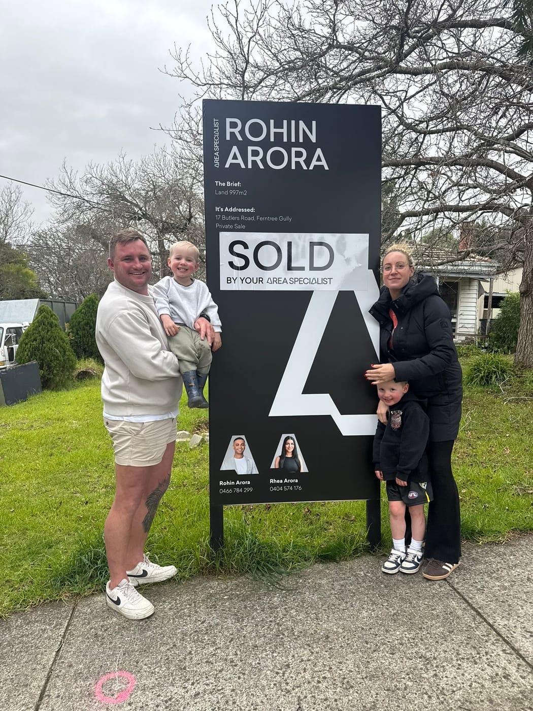 A family with two young boys beside a SOLD signboard