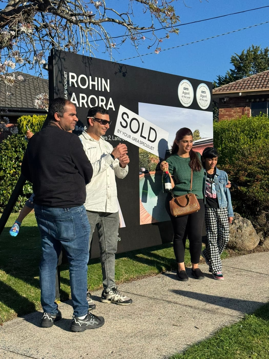 Family and friends holding up a SOLD sticker in front of a signboard