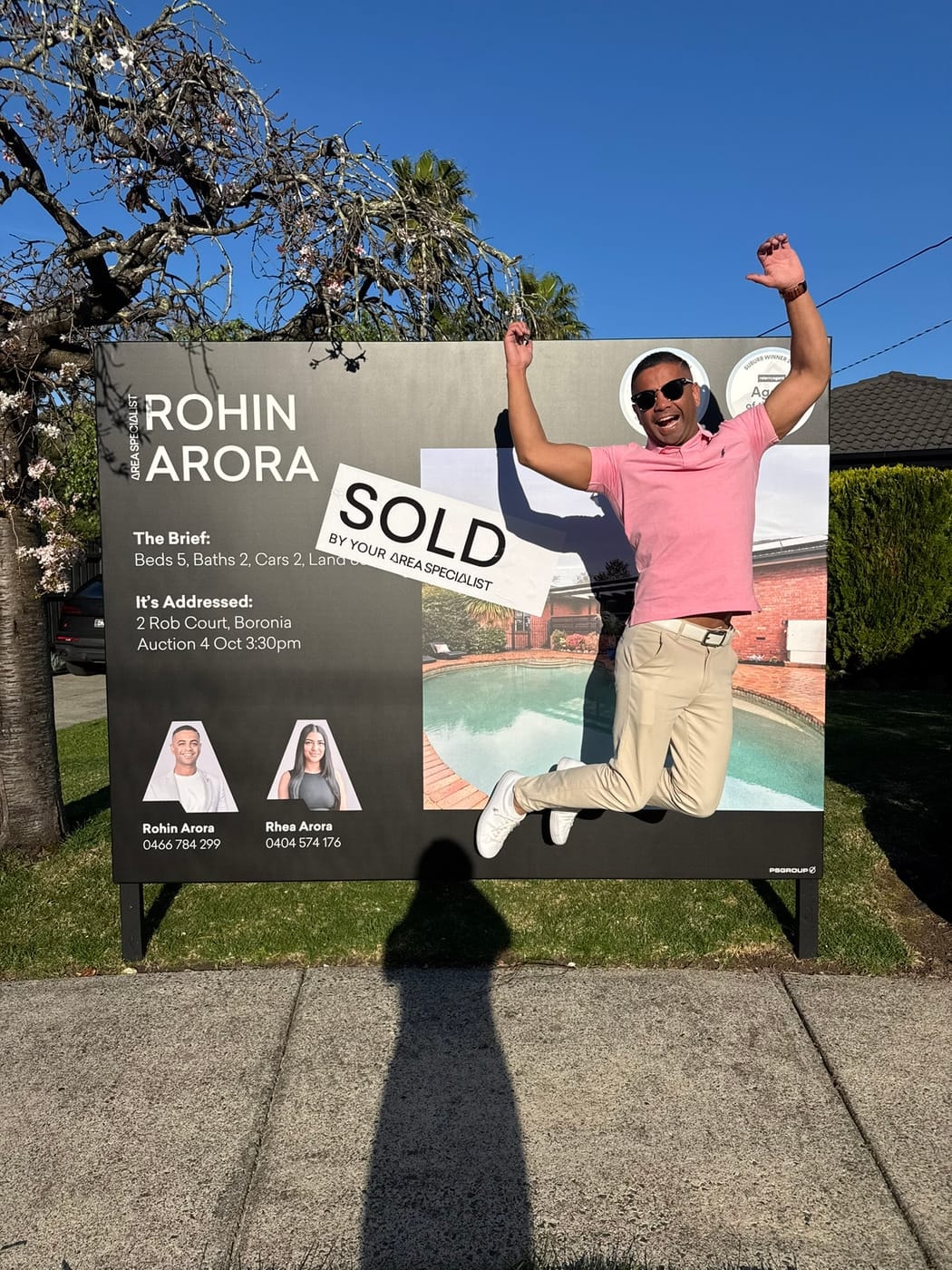 A man in a pink shirt leaping into the air in front of a SOLD signboard