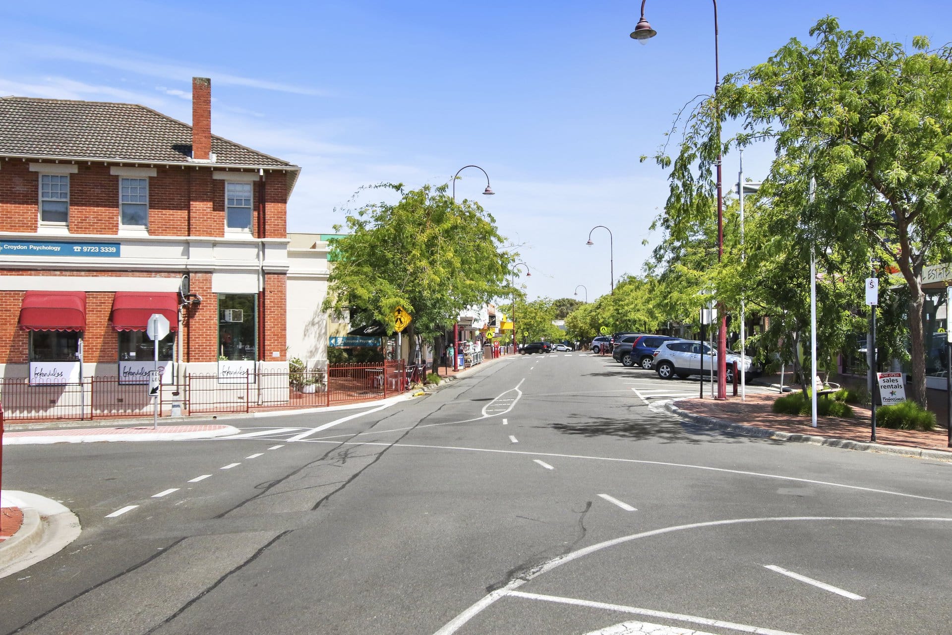 A two-storey red-brick corner building with red awnings, at the head of Croydon's tree-lined shopping street