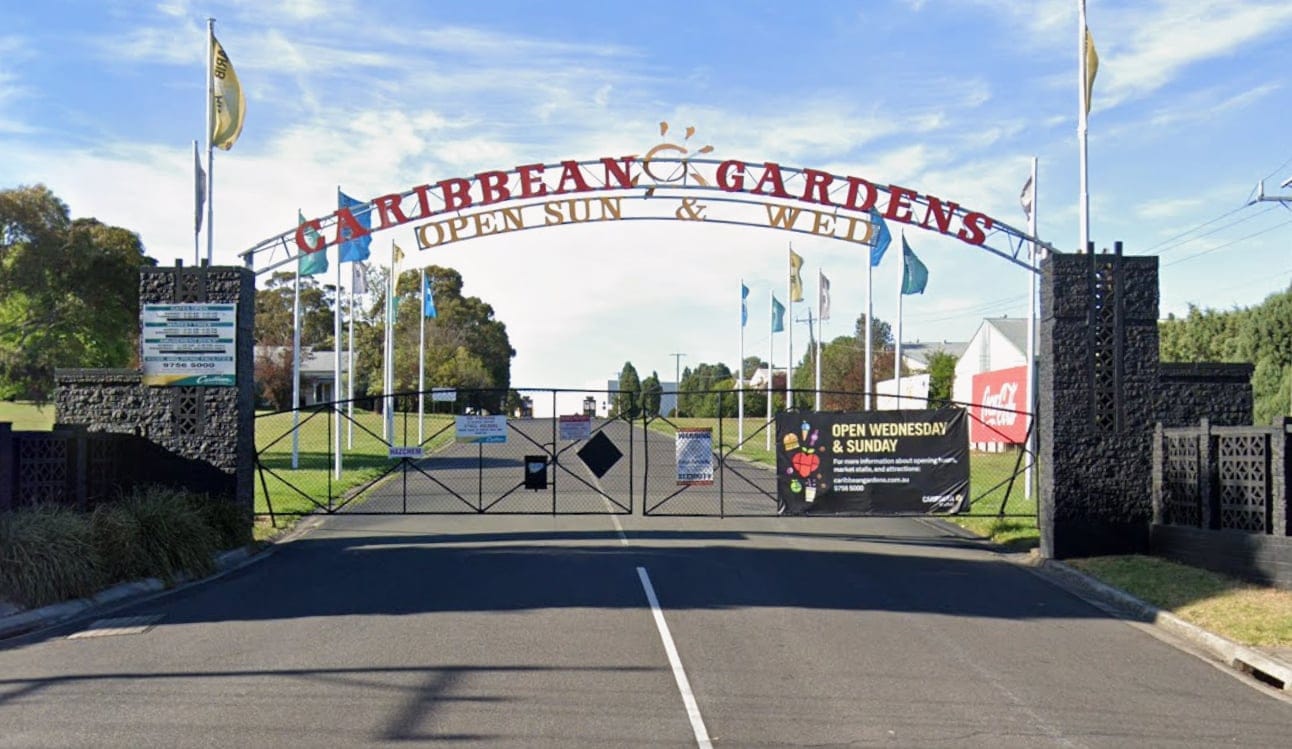 The Caribbean Gardens entrance in Scoresby: a lettered arch over closed gates, with flags lining the drive