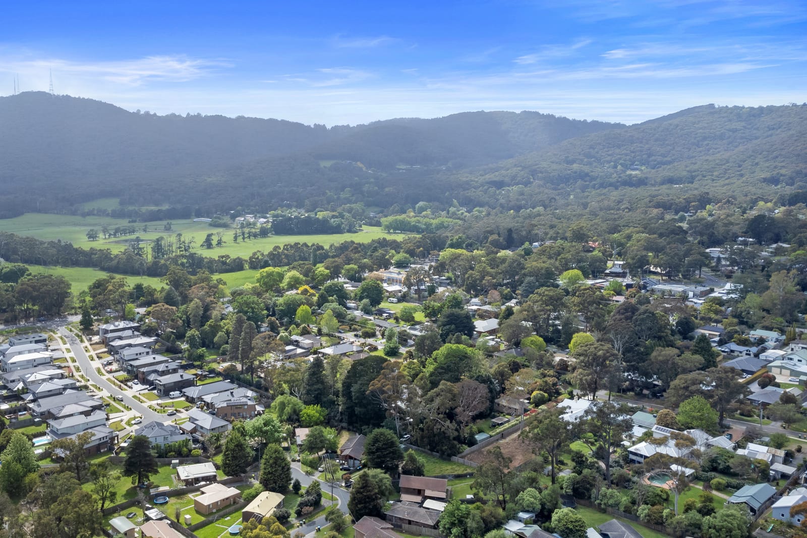 Aerial view over The Basin's houses and paddocks with the wooded Dandenong Ranges behind